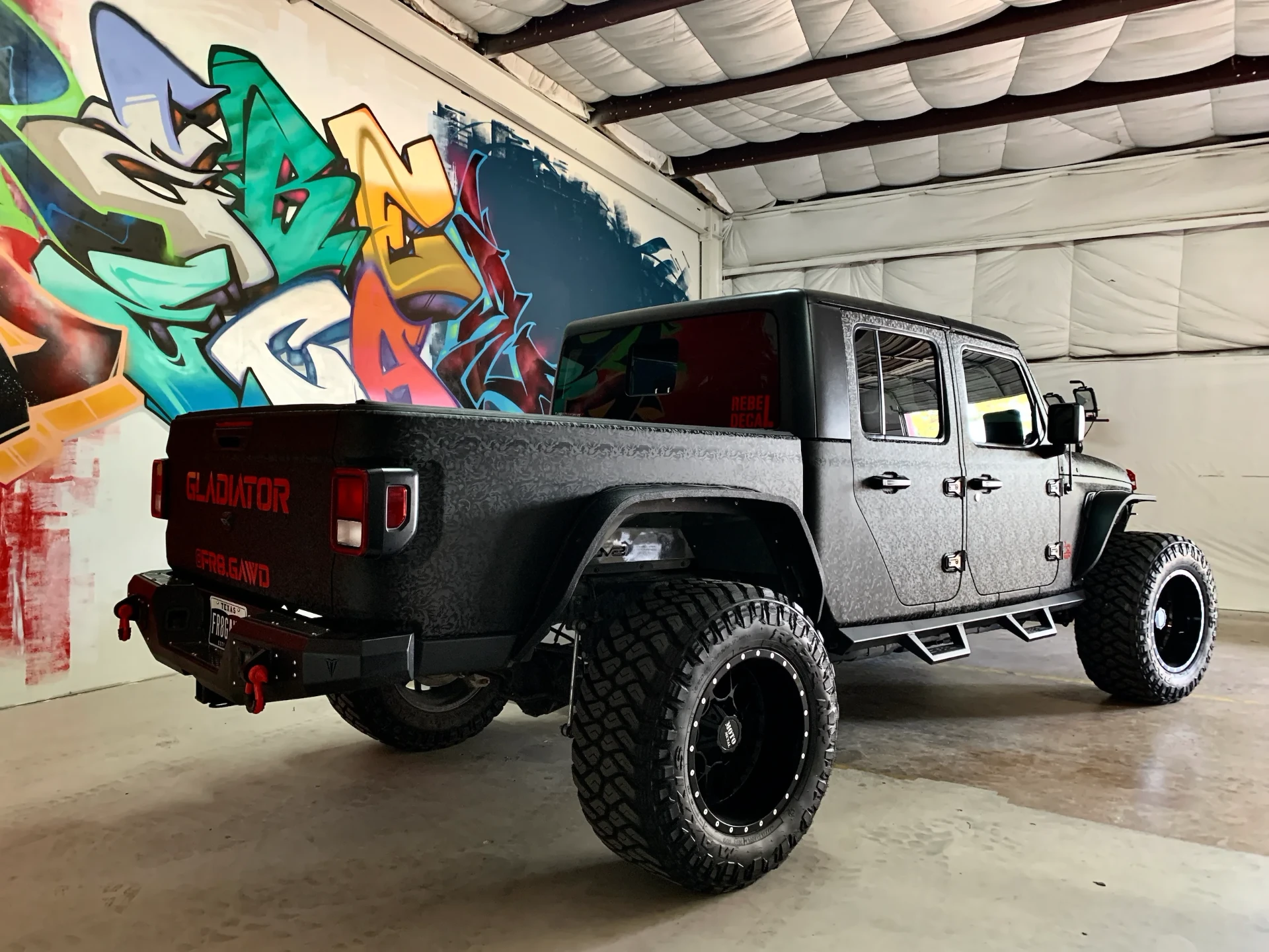 Custom Rebel Decal vehicle wrap on a lifted Jeep Gladiator inside the wrap facility